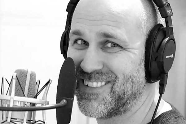 Swedish male voice-over talent with headphones, smiles behind microphone.