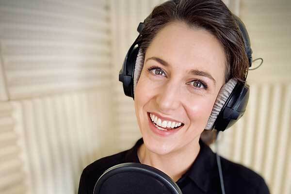 Scottish female voice-over talent smiling in home studio booth.