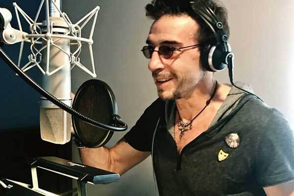 Spanish voice-over talent, smiles with glasses on, sitting behind mic.