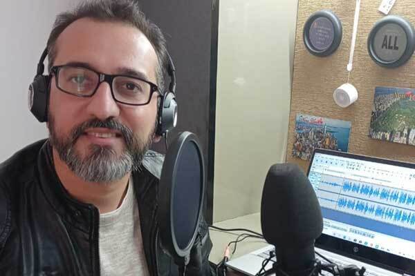 Male Indian voice-over talent with glasses and laptop in background.